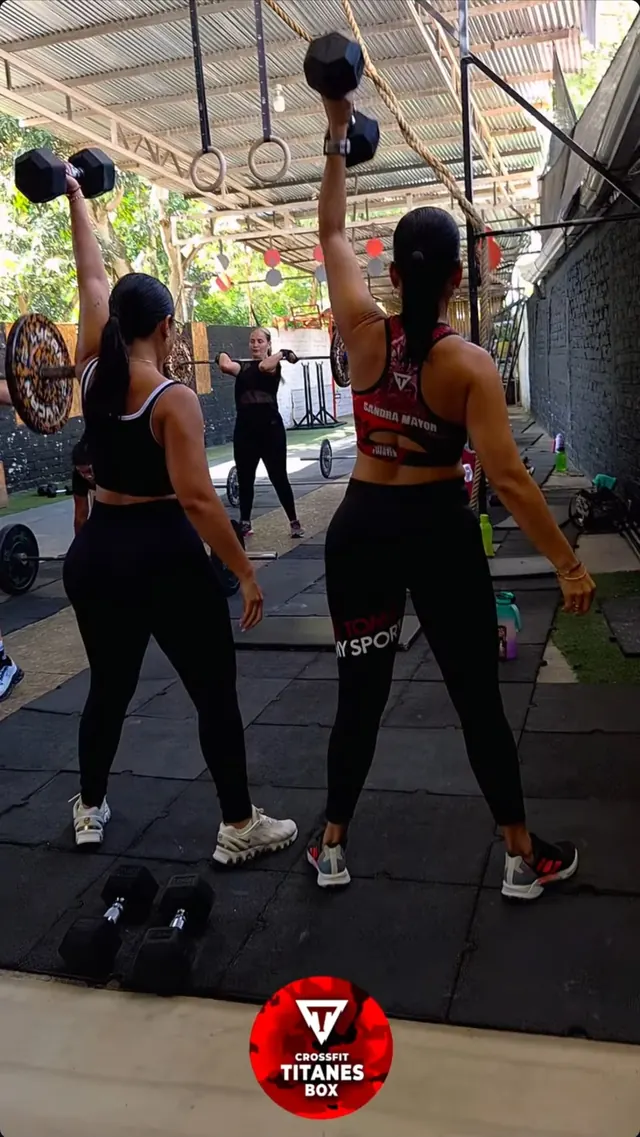 Dos atletas de Titanes Box levantan mancuernas sobre la cabeza durante una clase de CrossFit
