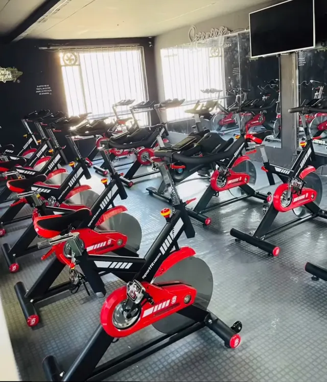 Sala de spinning de Titanes Box con bicicletas rojas y negras, ventanas y un televisor